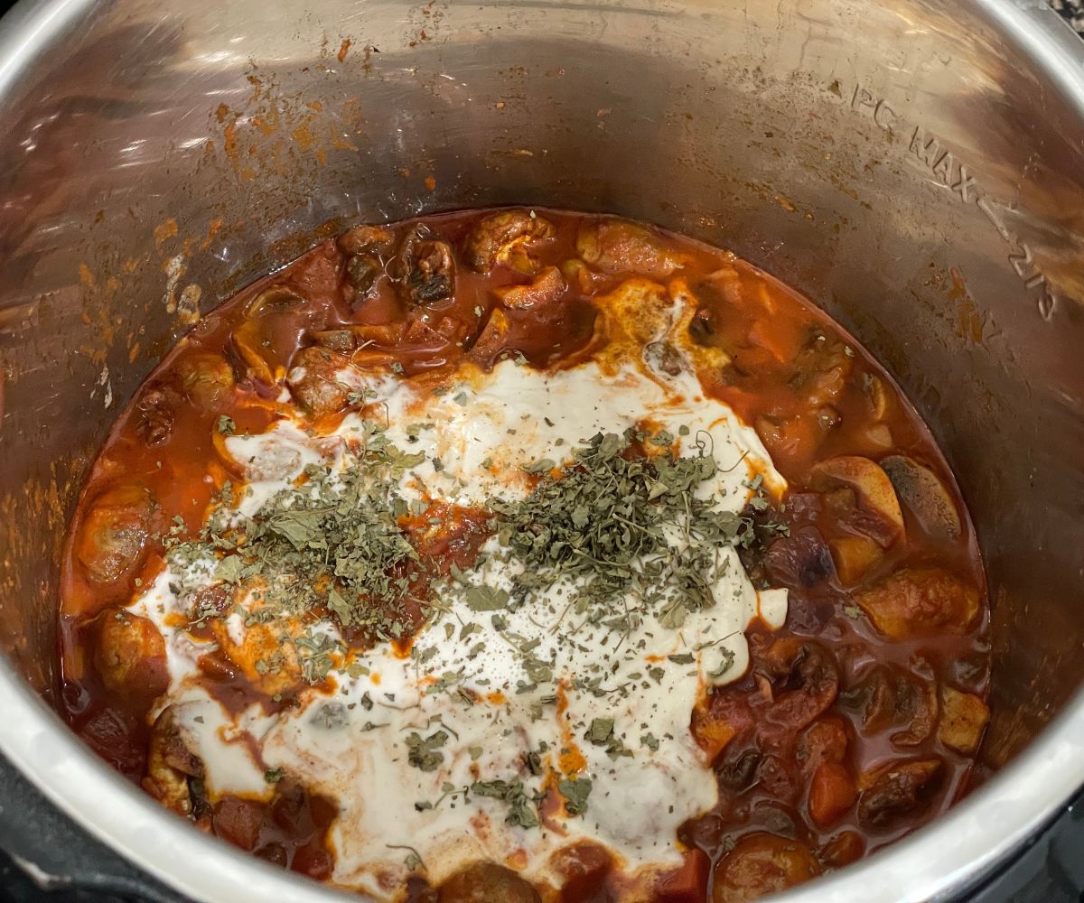 An instant pot is with mushroom curry and topped with kasuri methi and cashew cream.