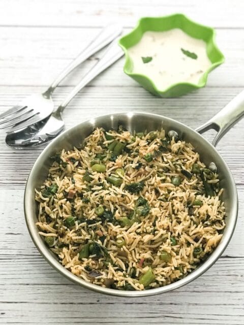 A pan is with spinach rice and bowl of raita on the table