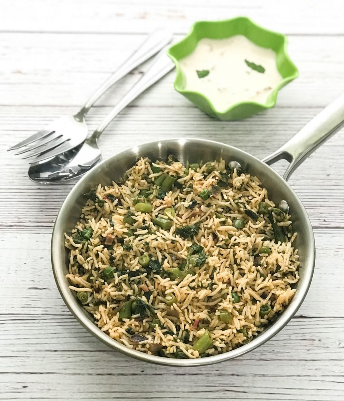 A pan is with spinach rice and bowl of raita on the table