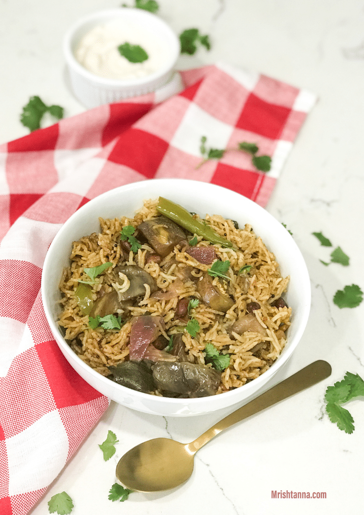 A white bowl filled with brinjal rice along with golden spoon