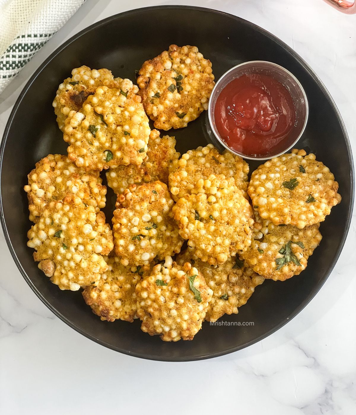 A plate of sabudana vadas is on the table along with tomato ketchup.