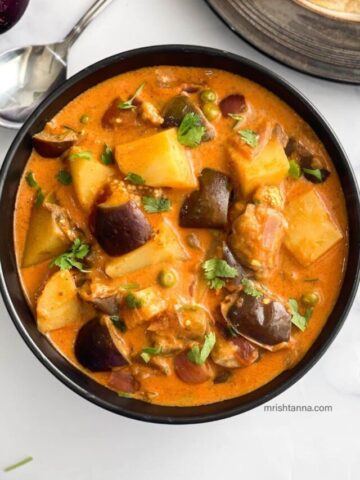 A bowl of Eggplant curry with potatoes is on the table.
