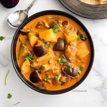 A bowl of Eggplant curry with potatoes is on the table.