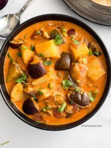 A bowl of Eggplant curry with potatoes is on the table.