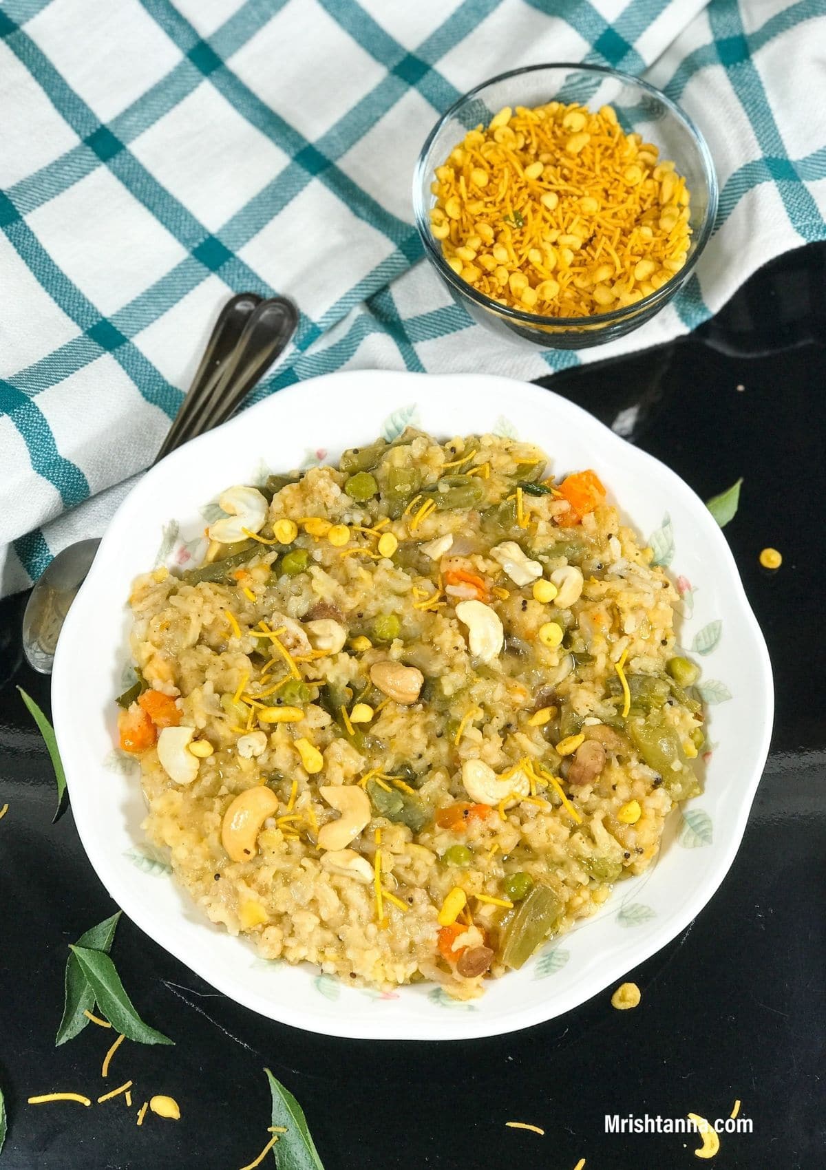 A plate of bisi bele bath is on the table and topped with nuts and boondi