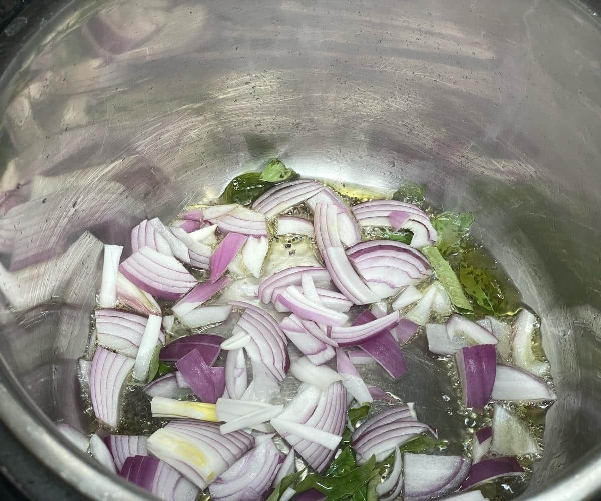An Instant pot is with spices and onions for Bisi Bele bhath recipe.