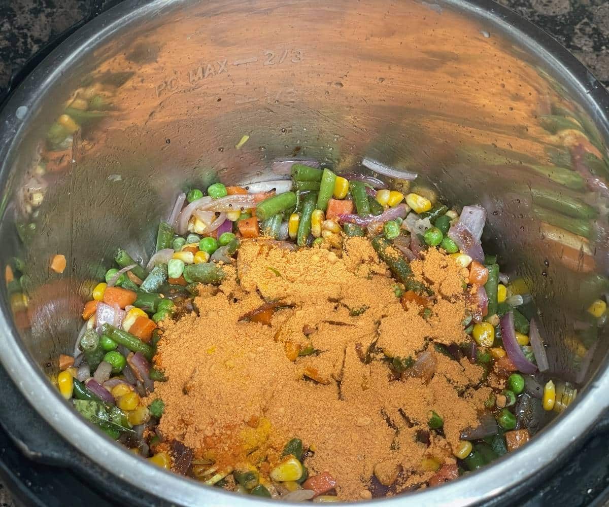 A pot has all the spices and veggies to cook Bisibelebath.