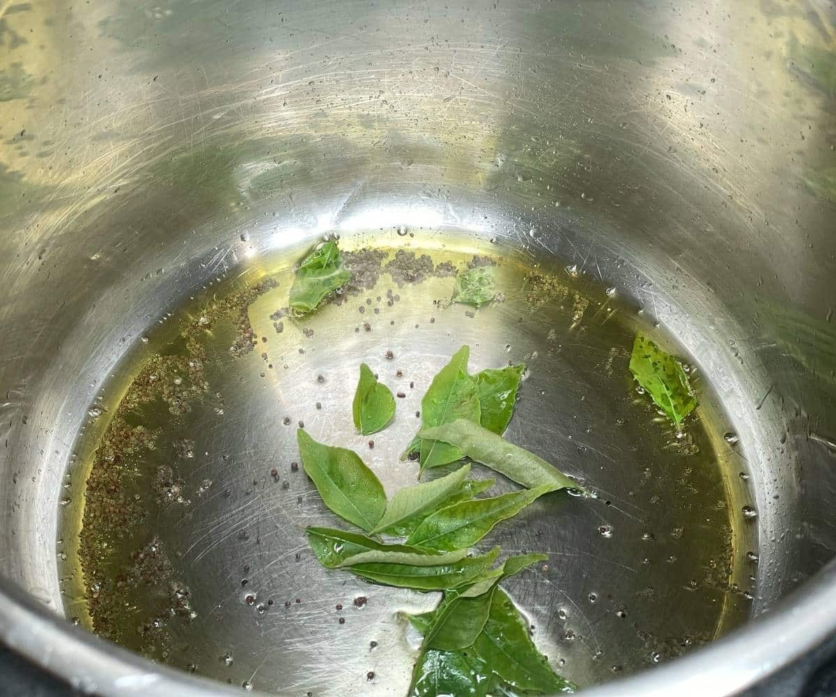 An Instant pot has mustard seeds and Curry leaves for Bisis bele bath recipe.