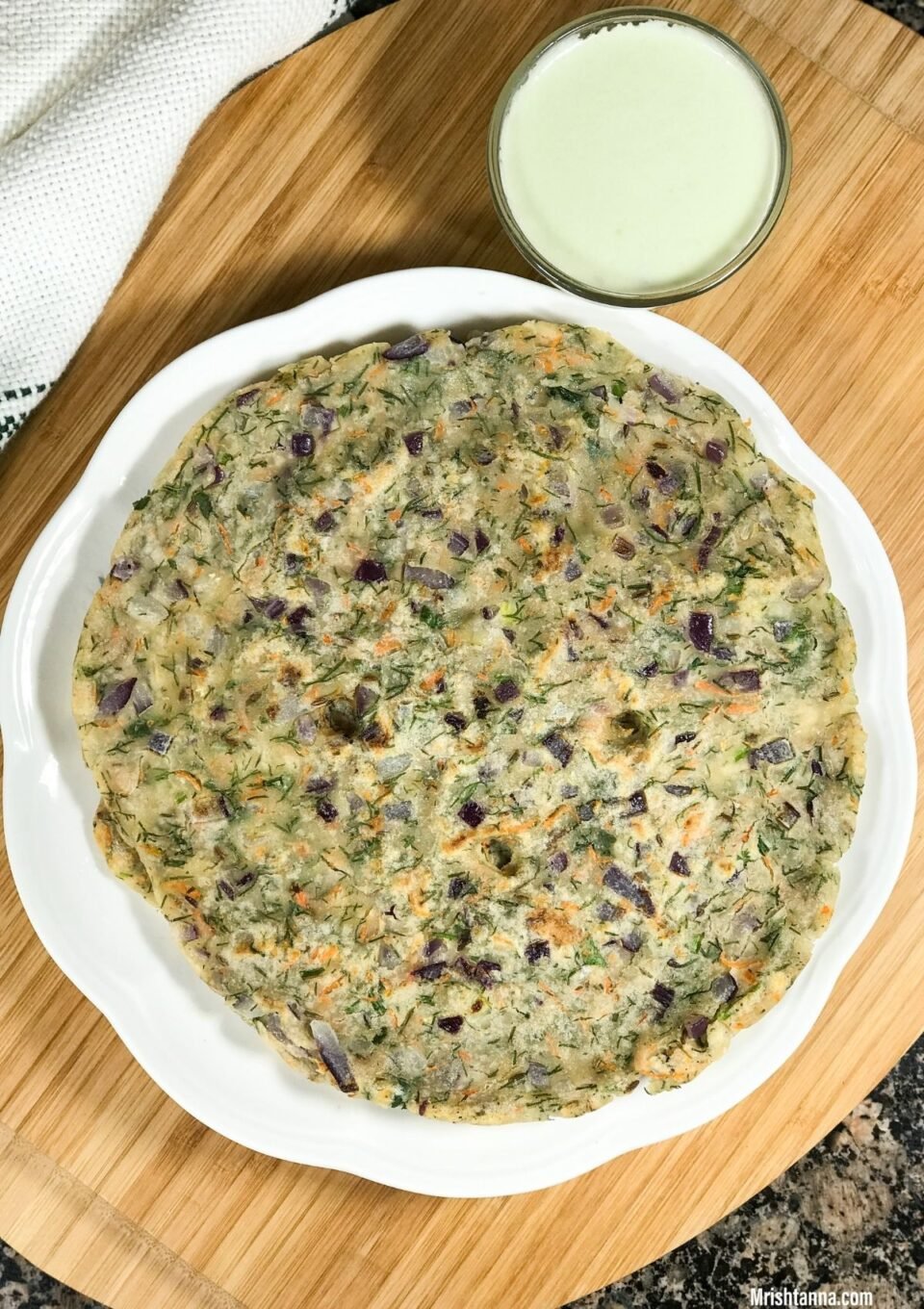 A white plate of akki roti and cup of chutney is on the wooden serving tray