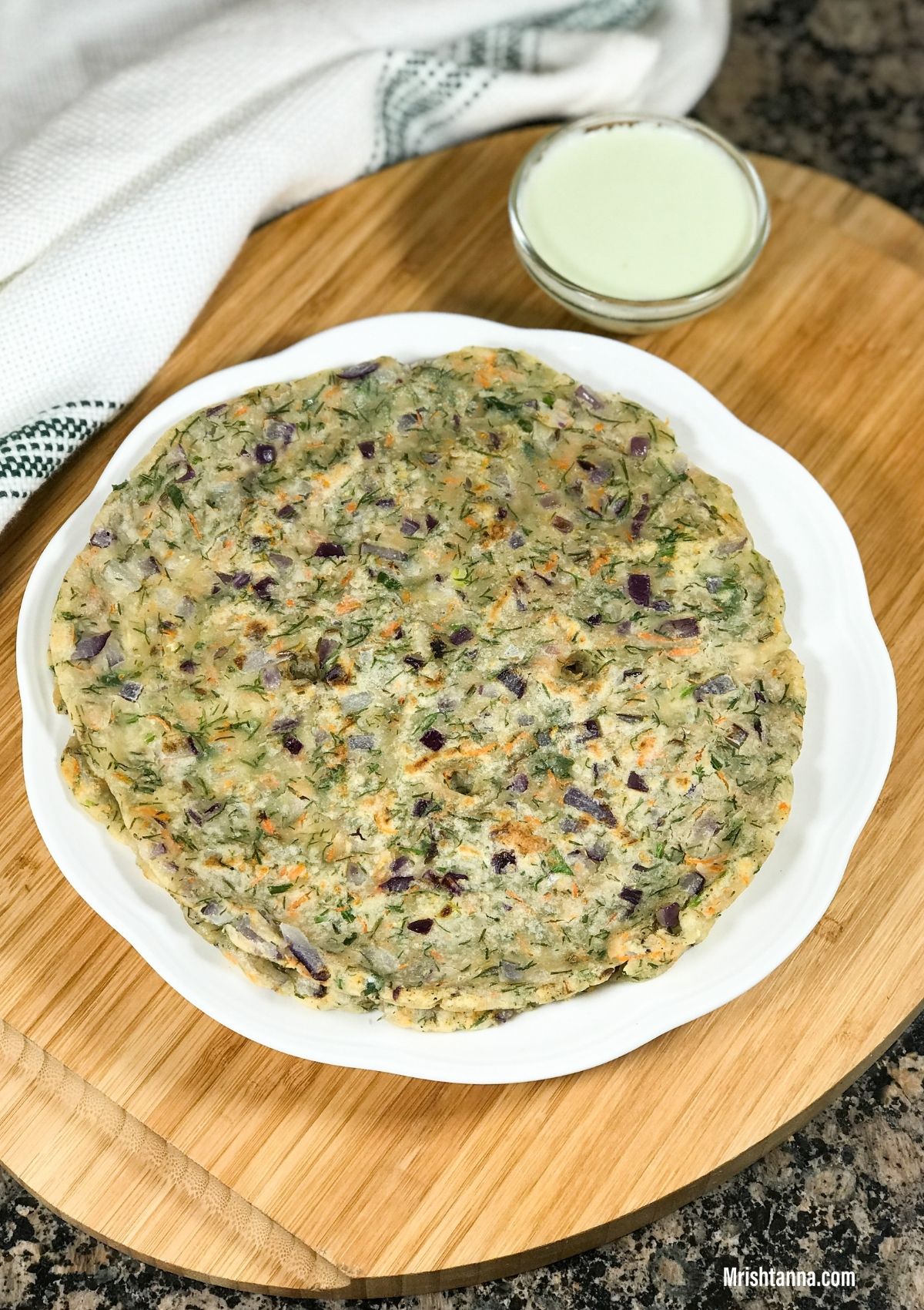 A plate with akki roti and a bowl of chutney is on the wooden table