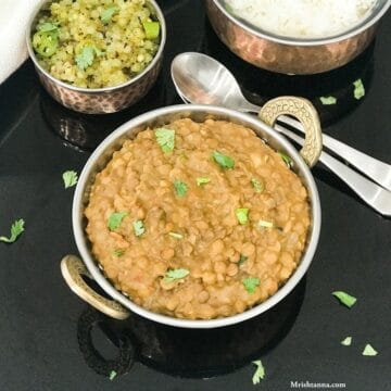 A bowl is filled with lentil curry and served on the black tray