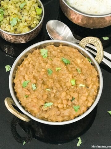 A bowl is filled with lentil curry and served on the black tray