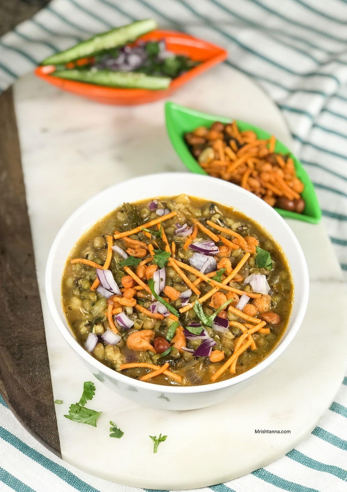 A bowl is filled with misal curry and topped with onions and fried mixture