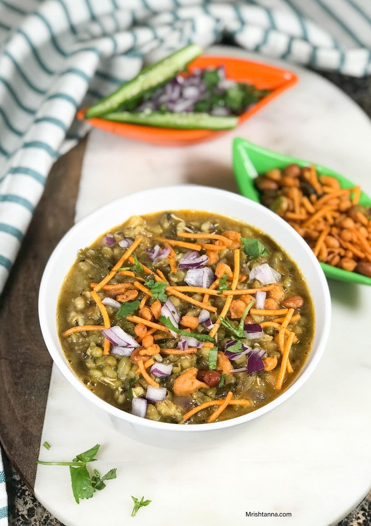 A white bowl with misal pav is on the serving tray along with chilies 