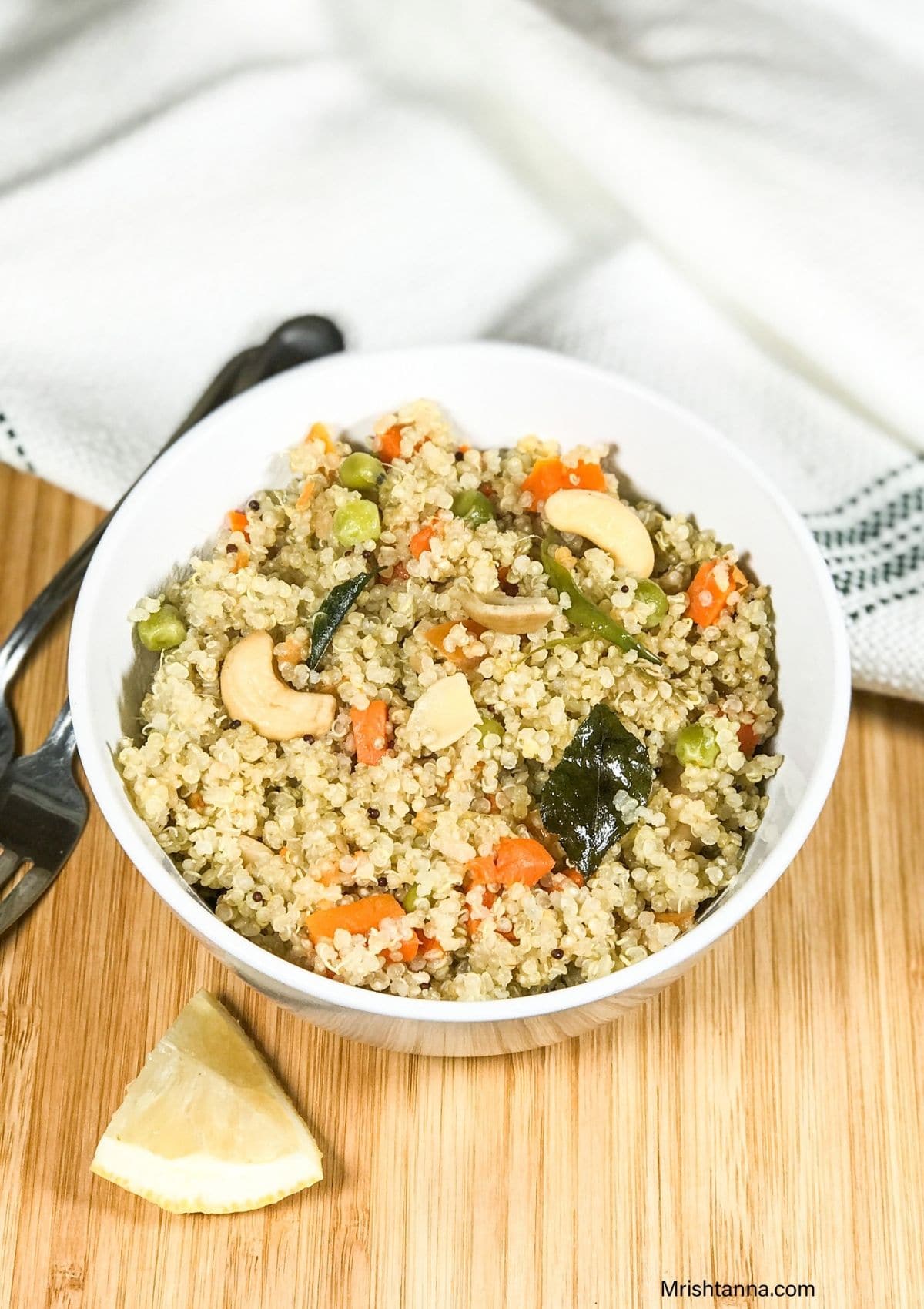 A bowl of quinoa upma along with sliced lemon and spoon