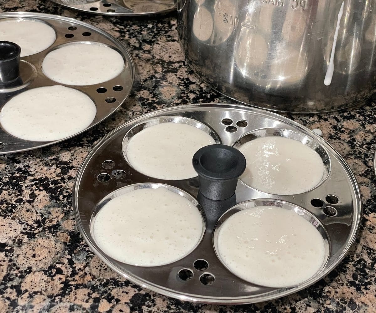 Idli batter is poured on the moulds.