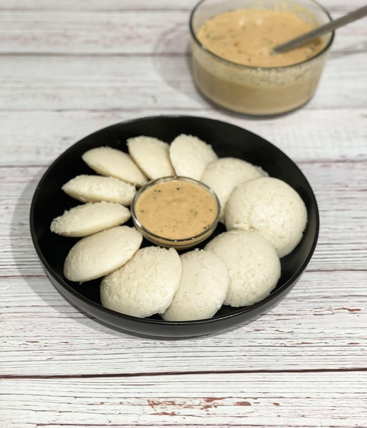 A plate of soft Idli's are on the table along with chutney.