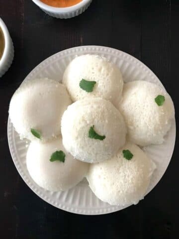 A plate with steamed idli's along with bowl of chutney and sambar is on the table