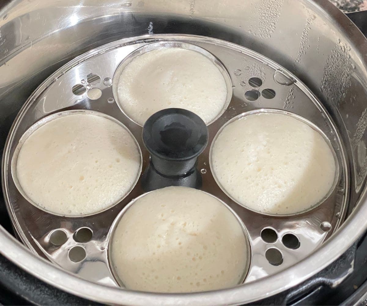 An instant pot is with steamed idli.