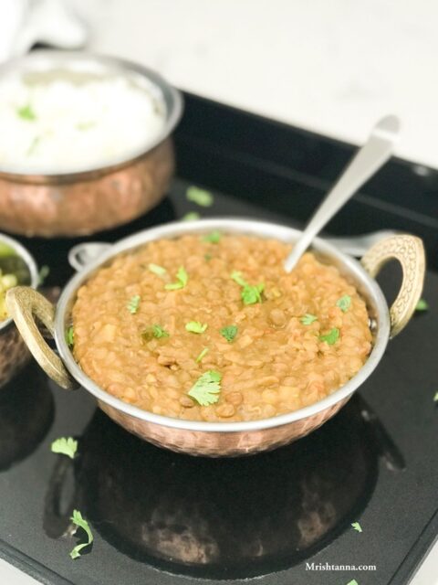 A bowl with lentil curry and spoon inserted and placed on the black serving tray