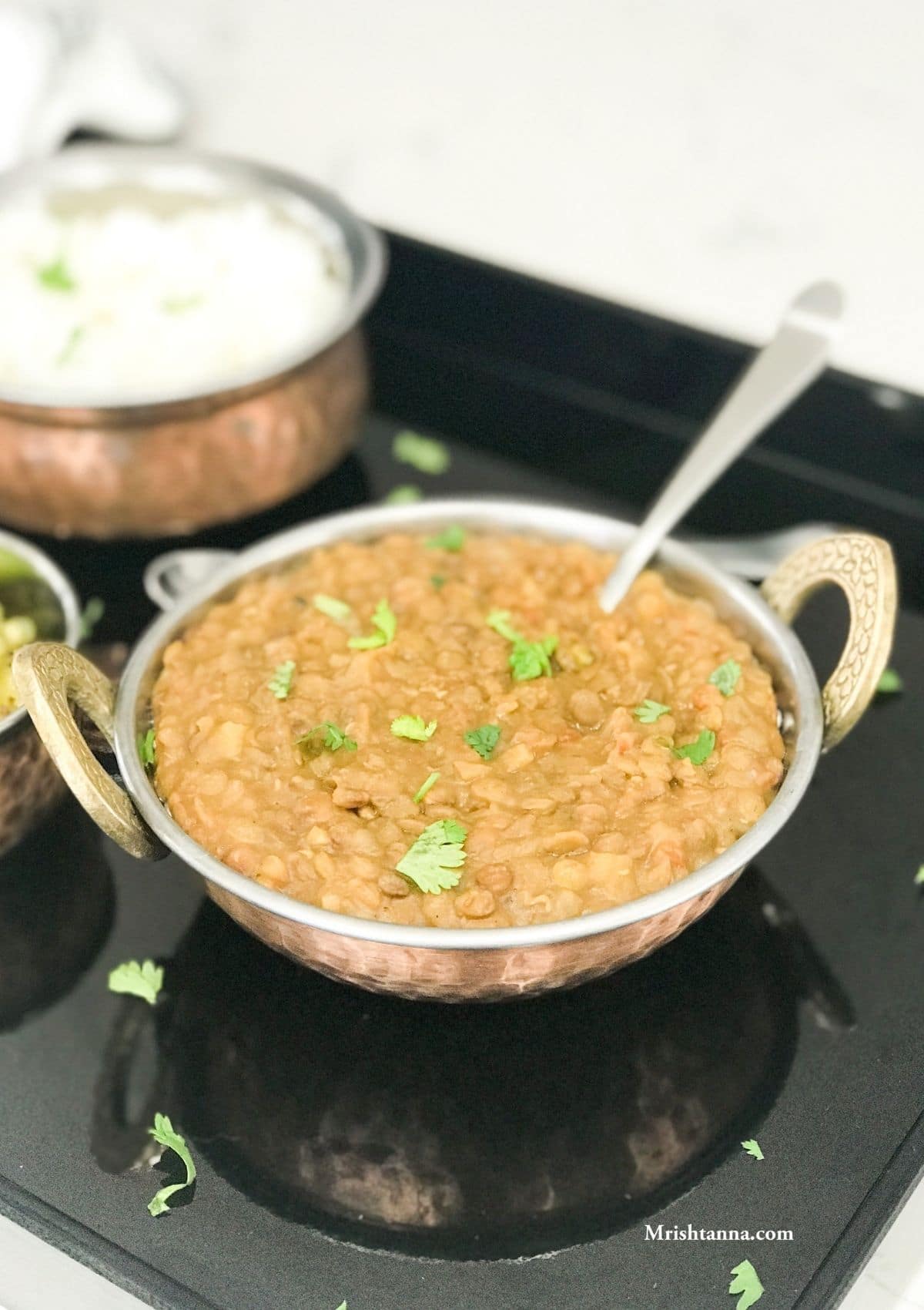 A bowl with lentil curry and spoon inserted and placed on the black serving tray