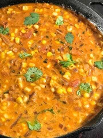 A cast iron pan with corn curry and topped with cilantro
