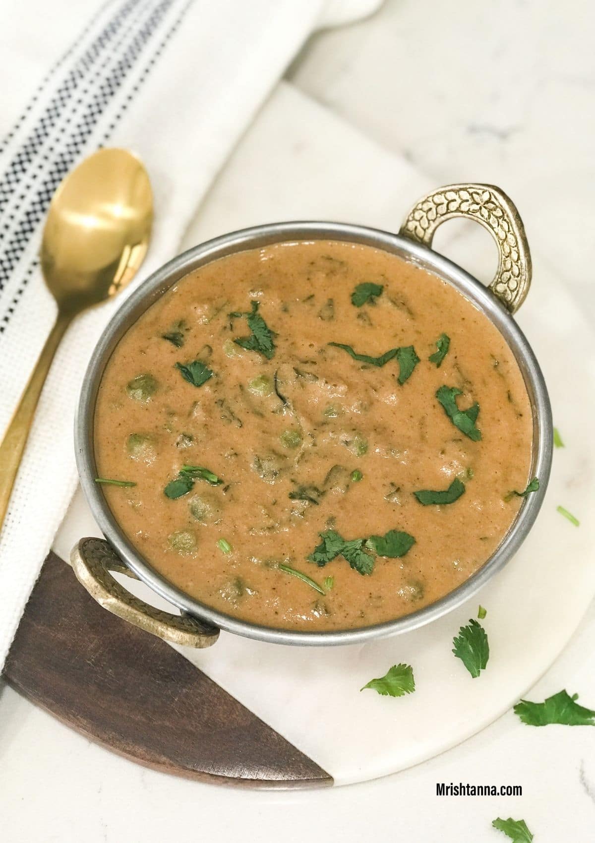 A bowl is filled with methi matar malai vegan curry and topped with cilantro