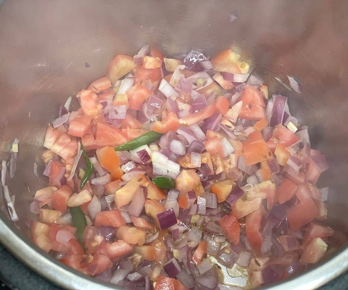 An instant pot is with tomatoes and onions on saute mode.