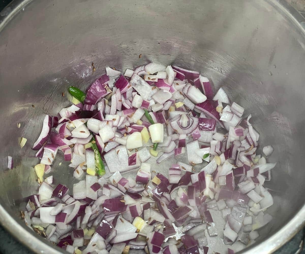 An instant pot has onions, ginger and green chilies for green moong dal.
