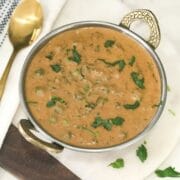 methi matar malai curry is served on the copper bowl and placed on the white table