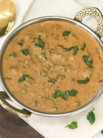 methi matar malai curry is served on the copper bowl and placed on the white table