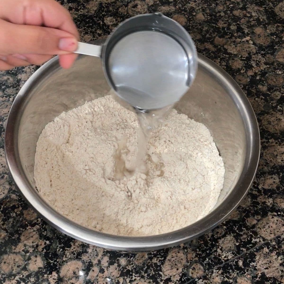A bowl is with wheat flour and water is pouring to the flour