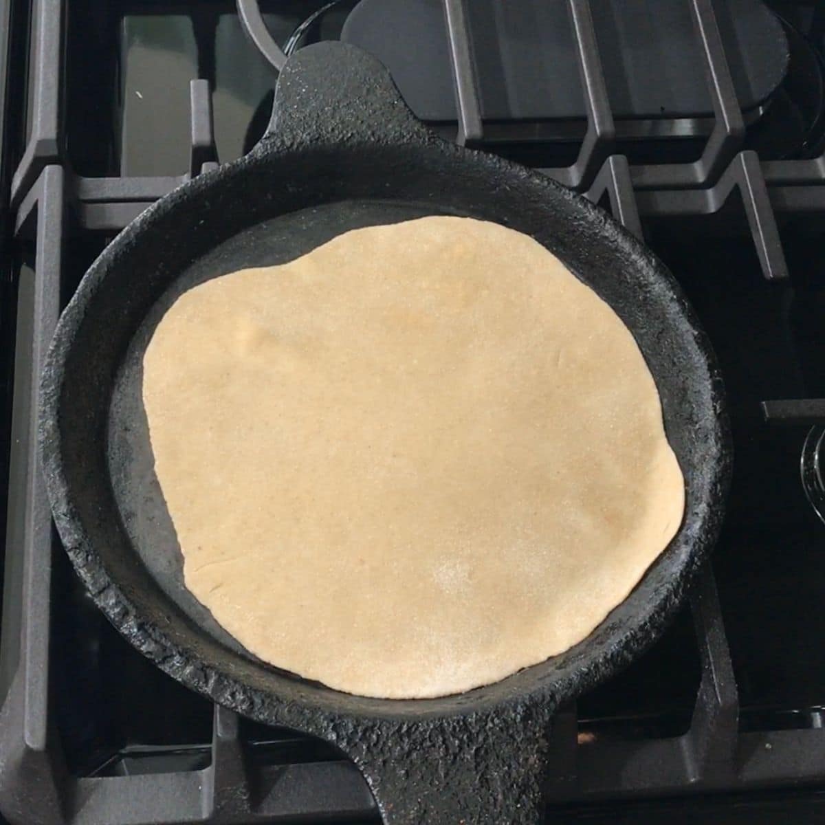 A phulka roti is placed on the tawa over the heat