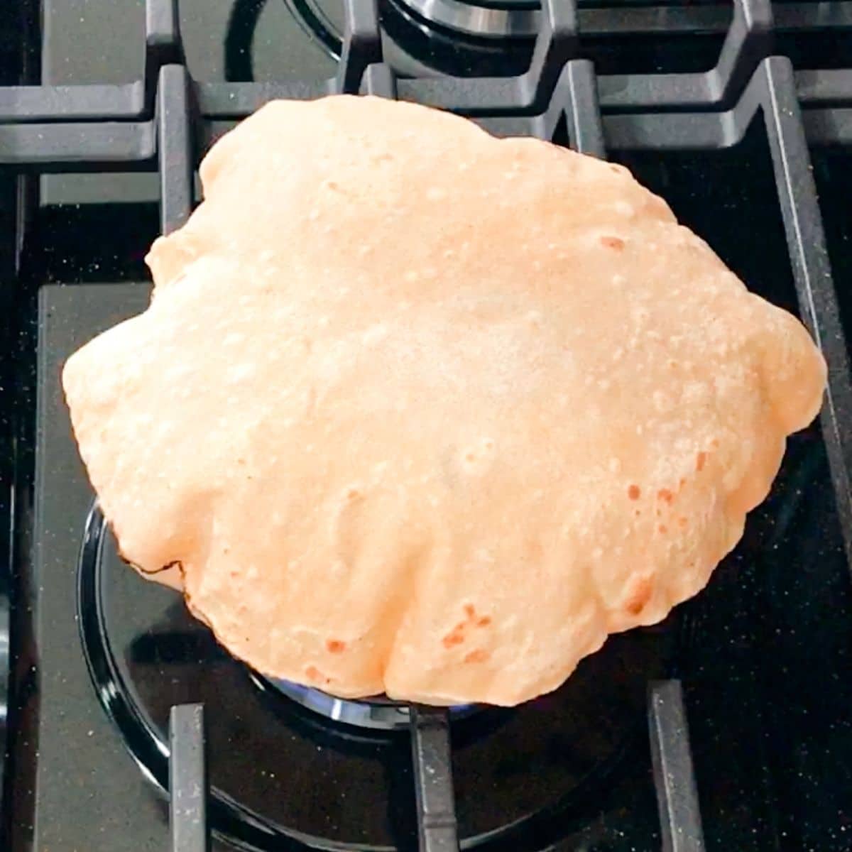 A Phulka roti is puffed up on the stove top