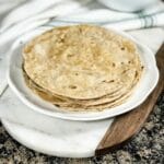 Phulka roti is stacked on the white plate and on the serving tray