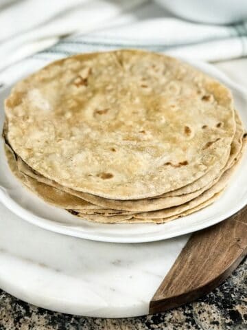 Phulka roti is stacked on the white plate and on the serving tray