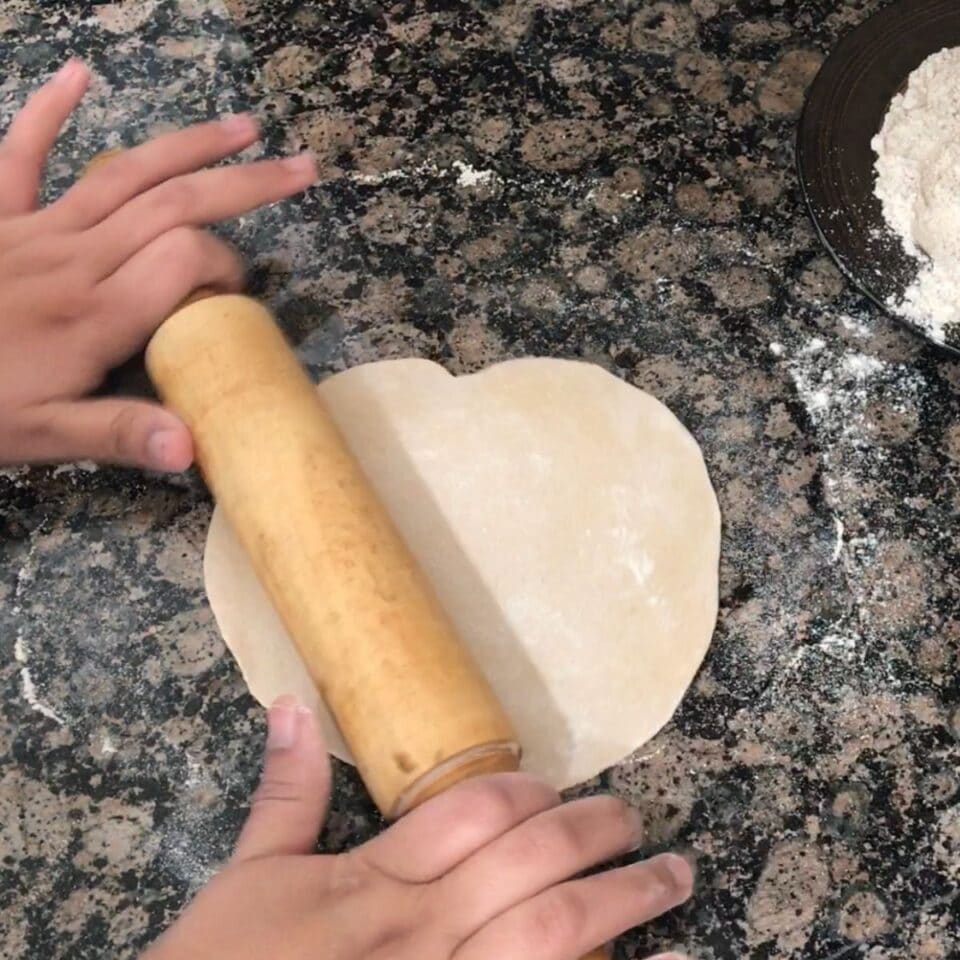 Roti dough is rolling  on circular shape by a lady.