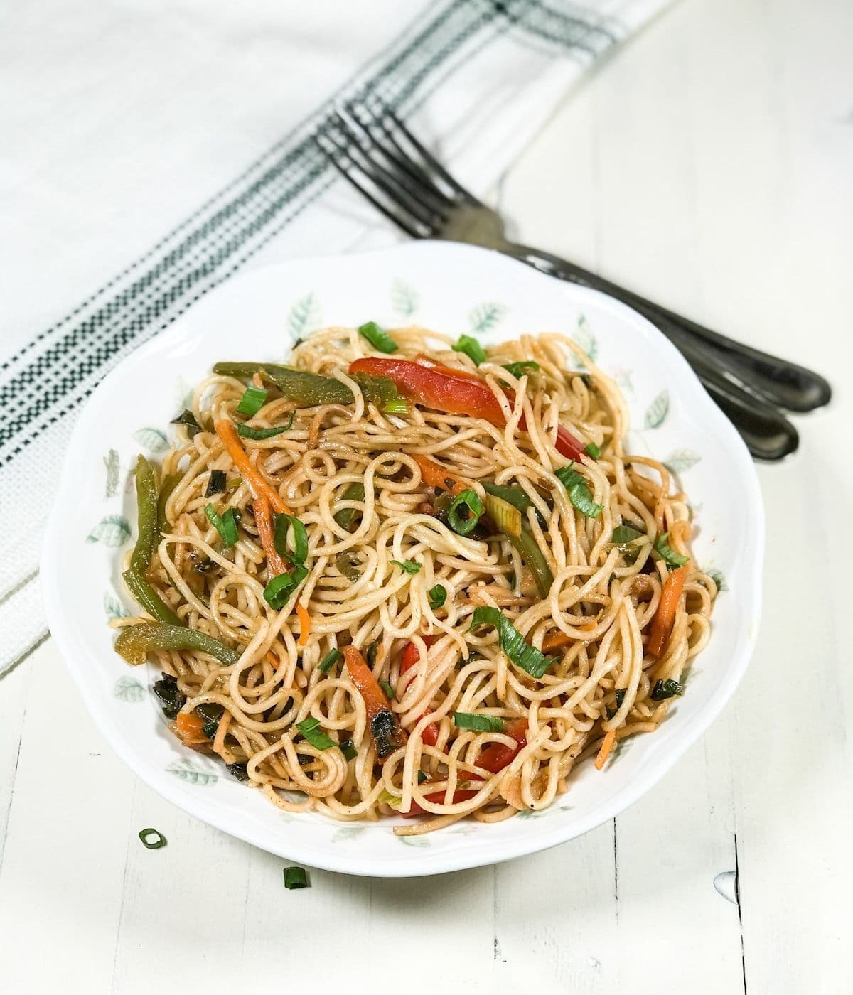 A plate with hakka noodles and topped with spring onions on the table