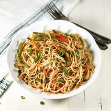 A plate is filled with vegetable hakka noodles and placed on the white table