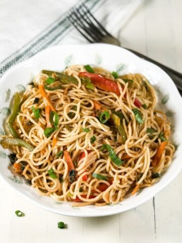 A plate is filled with vegetable hakka noodles and placed on the white table