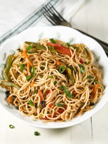 A plate is filled with vegetable hakka noodles and placed on the white table