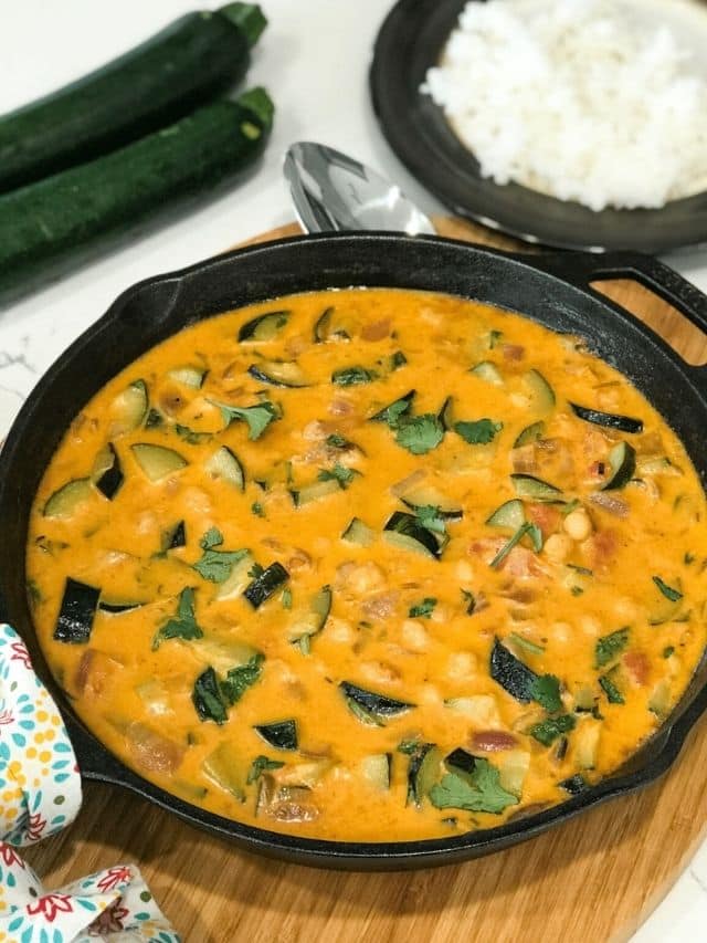 A cast iron pan is filled with zucchini curry and topped with cilantro leaves