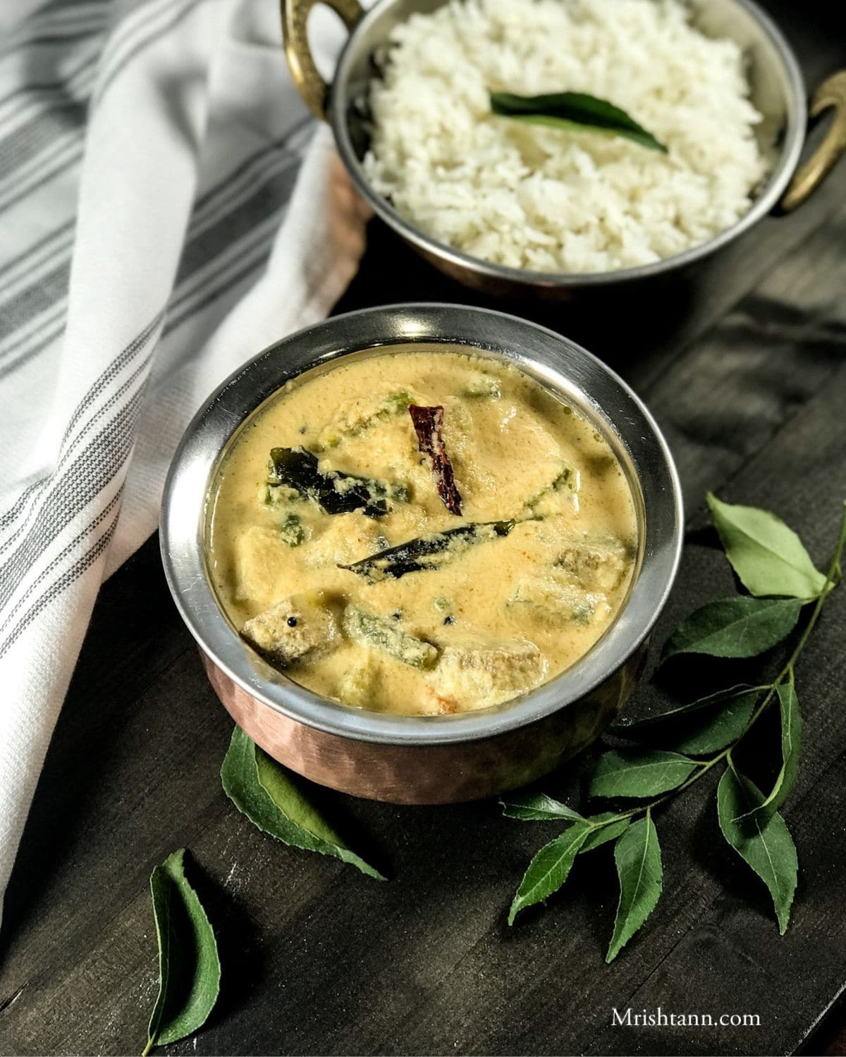 A copper bowl is with aviyal curry and topped with tempering