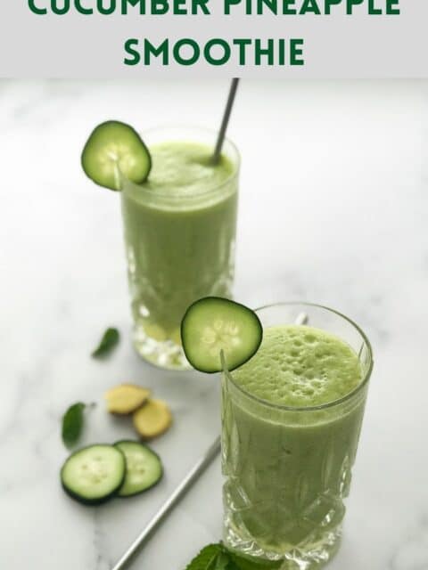 Two glasses are filled with cucumber smoothie and placed on the white surface along with straws.
