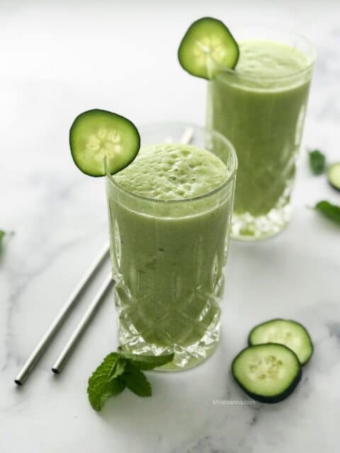 Two glasses of cucumber pineapple smoothies are over the white table
