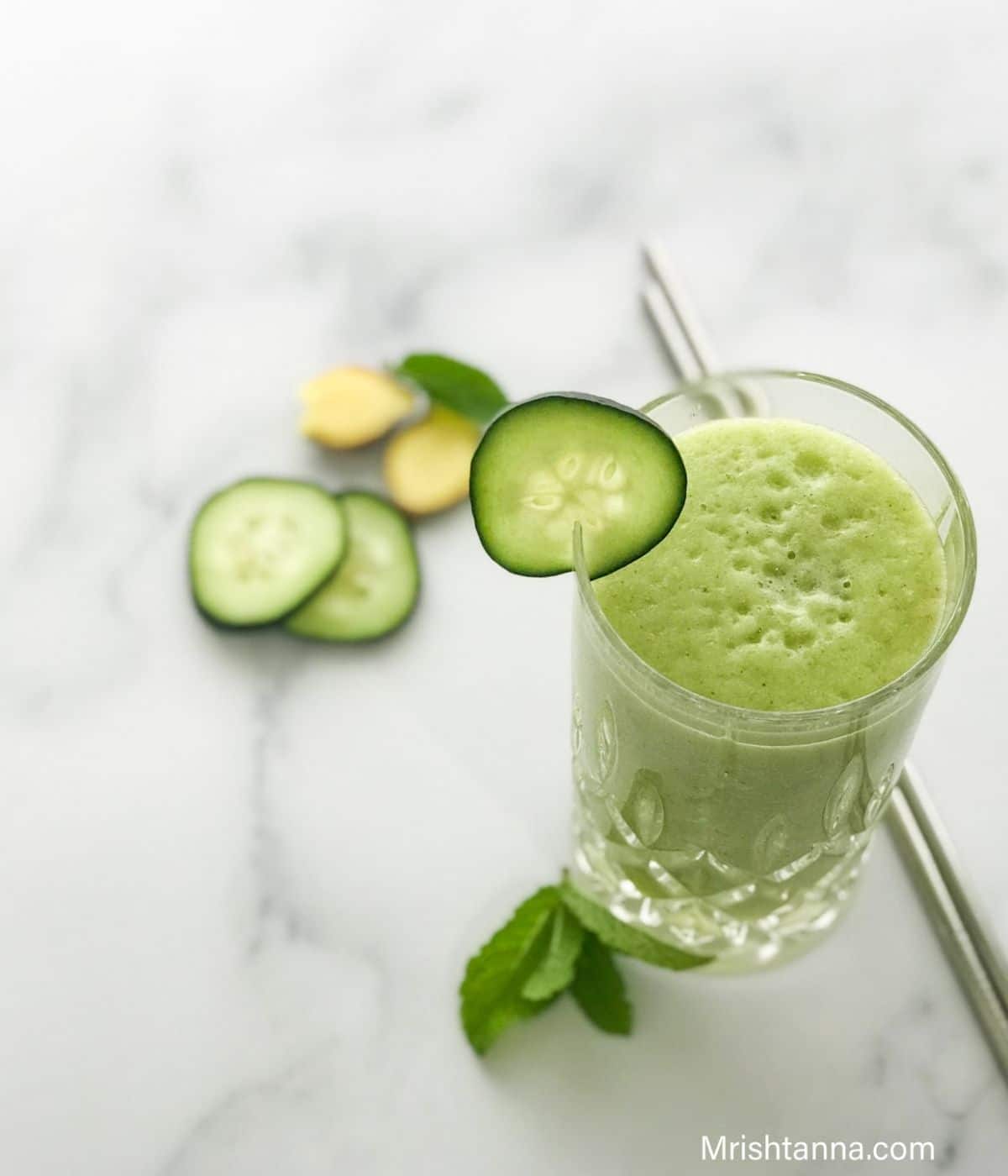 A tall glass is filled with smoothie and cucumber slices are placed on the side