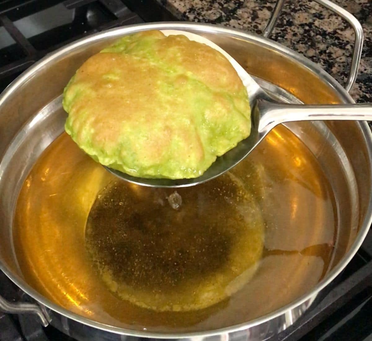 A laddle with fried puri over the stove top