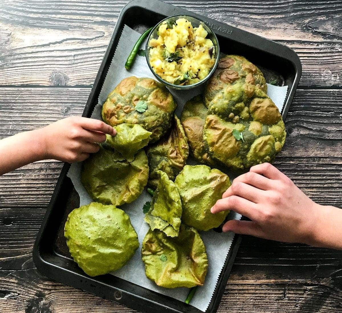 kids picking up the palak puri from the tray over the table.