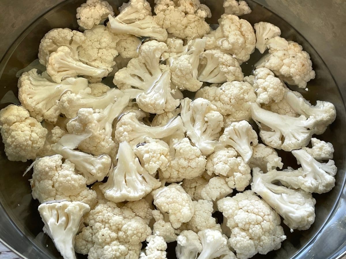 A bowl is with hot water and cauliflower on the table