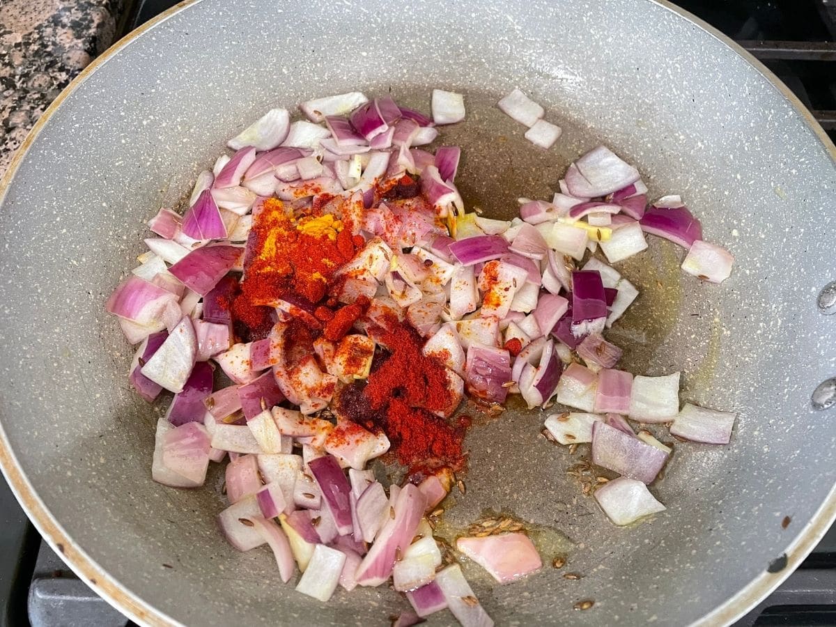 A pan is over the stove top and its filled with onions and spices